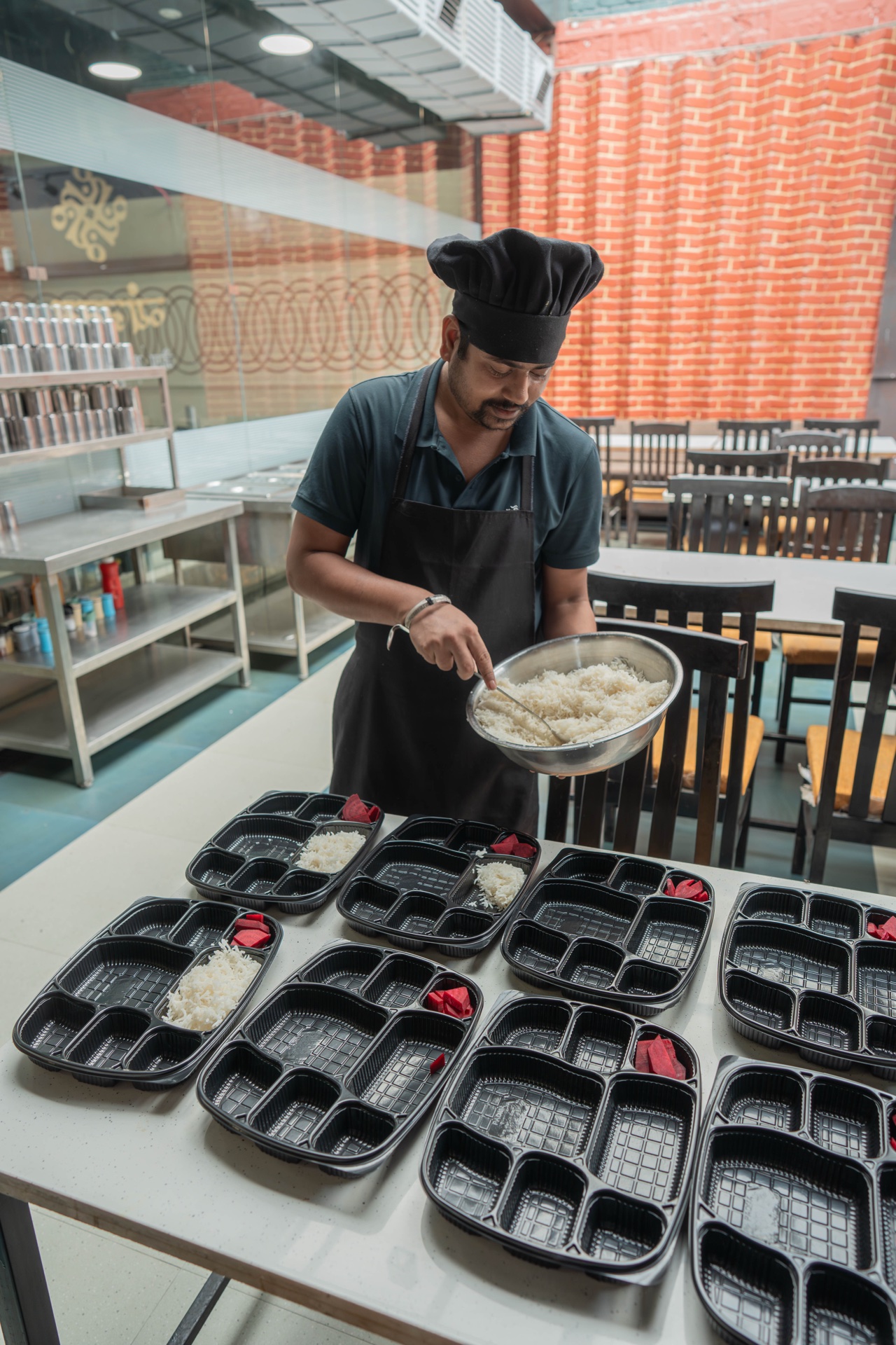Chef portioning fresh rice into compartment meal trays at Vyanjanam