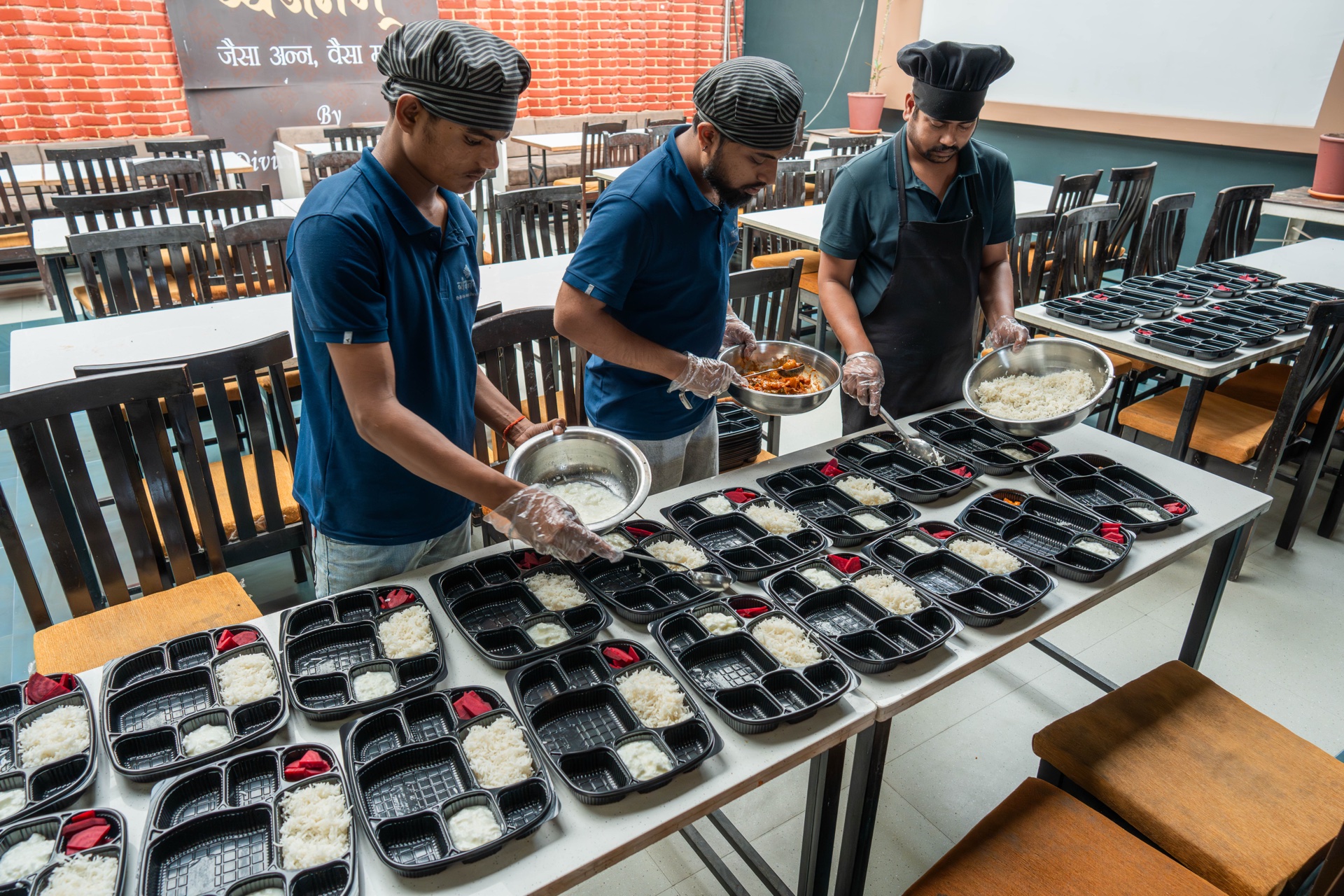 Vyanjanam kitchen team filling meal trays in an assembly line