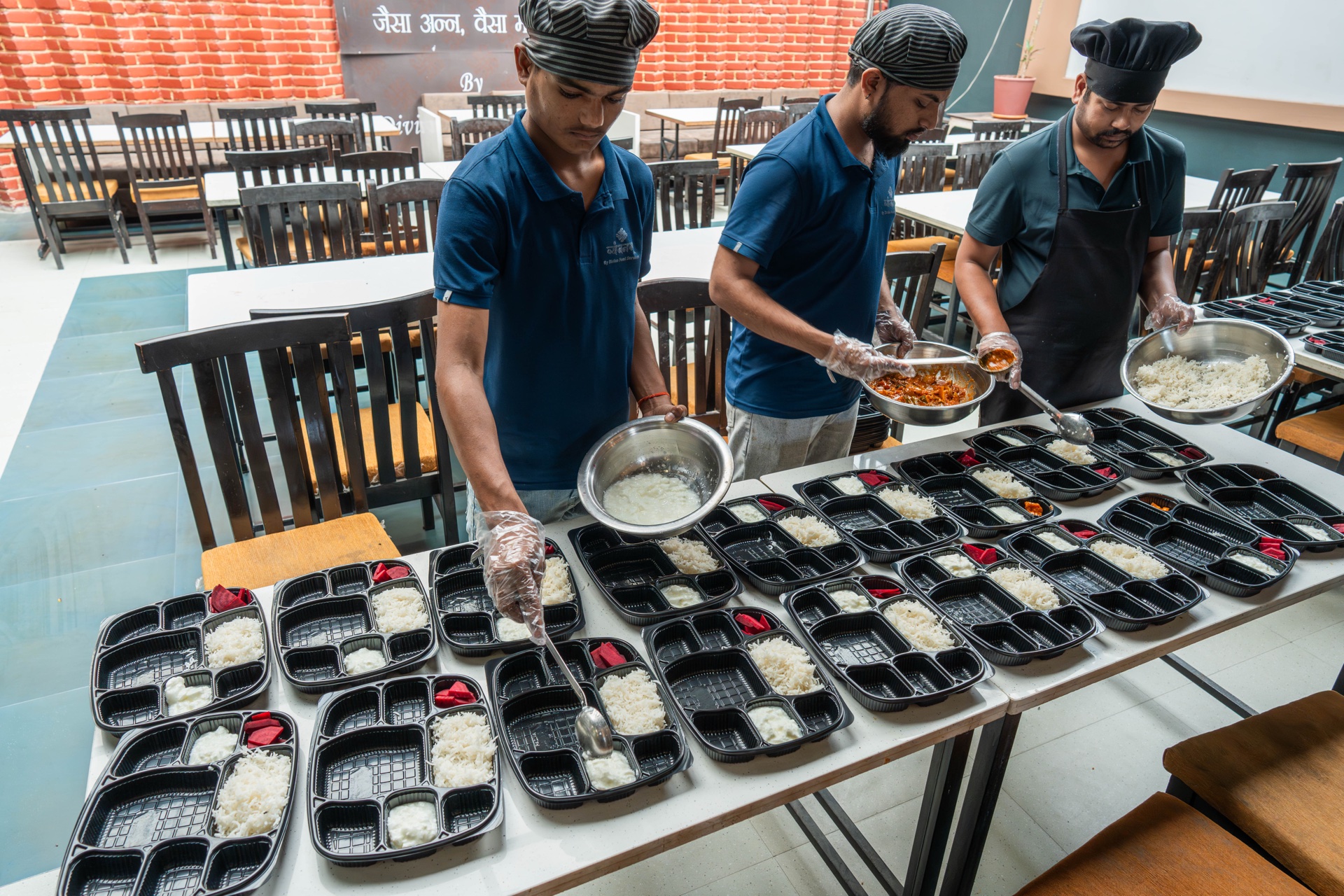 Team plating rice, curd and curry into meal trays at Vyanjanam